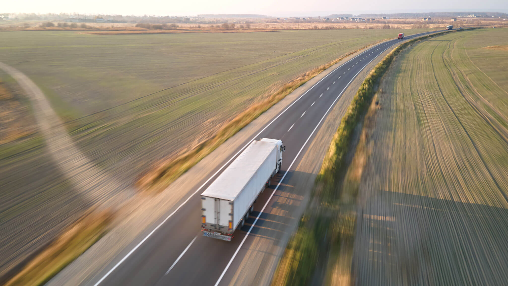 Aerial View Of Blurred Fast Moving Semi Truck With Cargo Trailer Driving On Highway Hauling Goods In Evening. Delivery Transportation And Logistics Concept
